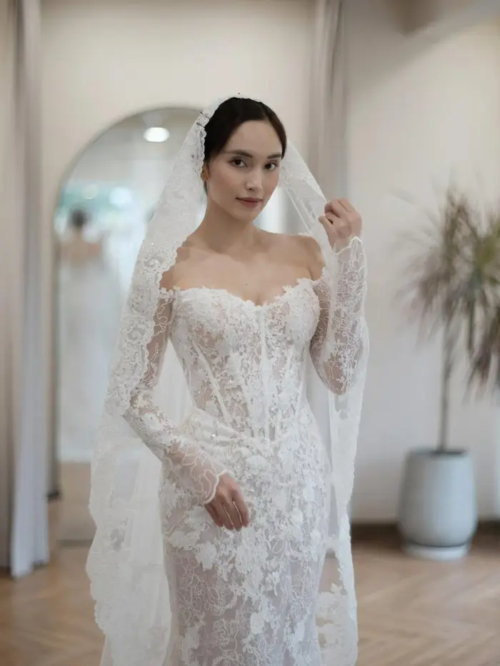 Fitting-room reference — bride trying a similar off-the-shoulder lace mermaid at a bridal studio, sent to Vi