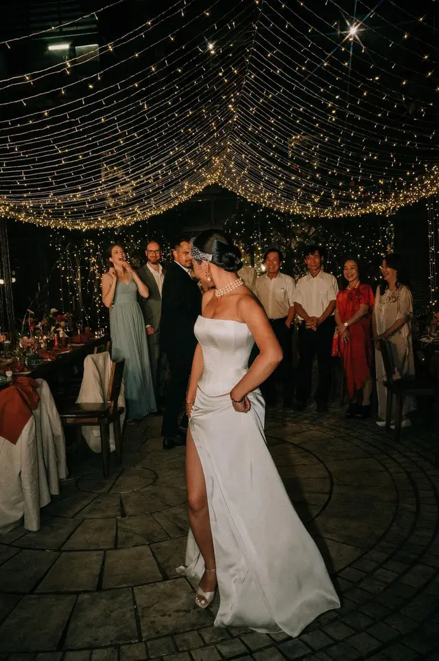 Bride in a custom VI Dressmakers strapless ivory satin corset split Aline look with thigh-high slit at an outdoor evening reception under warm fairy lights